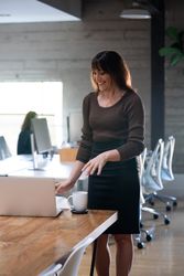 Transgender woman in knitted top and skirt standing with laptop in open plan office