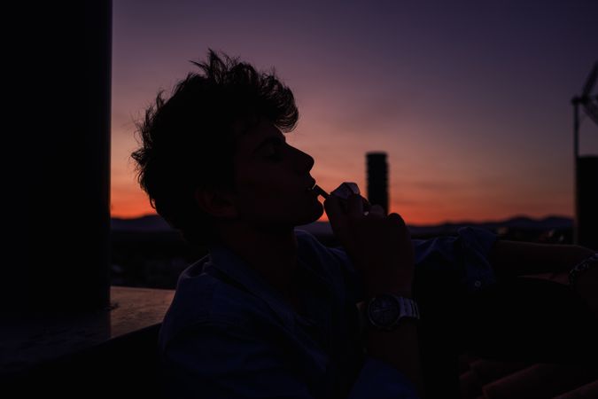 Young man smoking cigarette during sunset