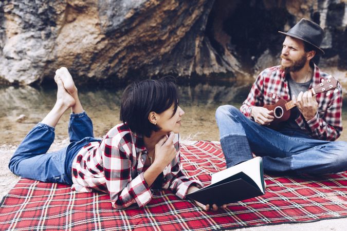 Chilling couple with book and guitar on shore