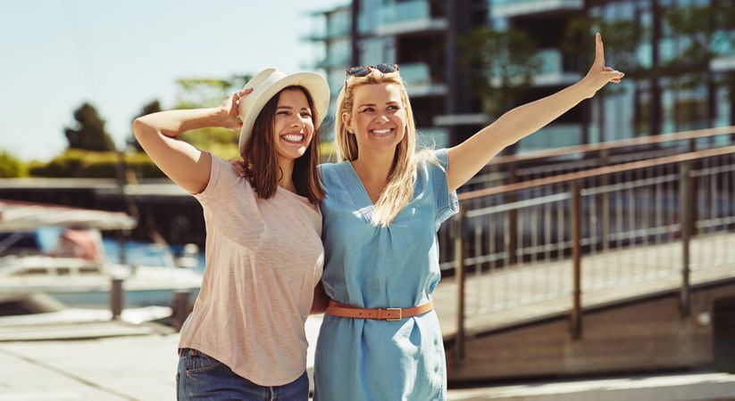 Two women happily walking together on sunny day next to river, copy space