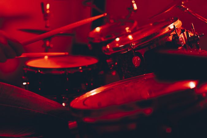 Anonymous man with drumsticks playing on drums in redness
