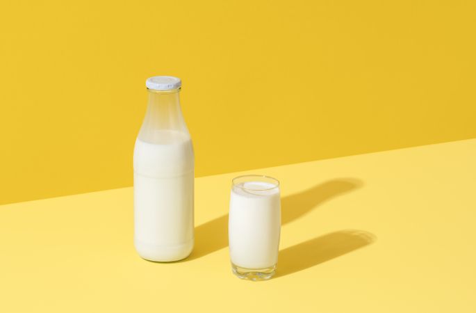 Milk in glass and bottle, minimalist on yellow background
