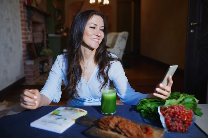 Woman at the table with healthy food making mobile photo selfie