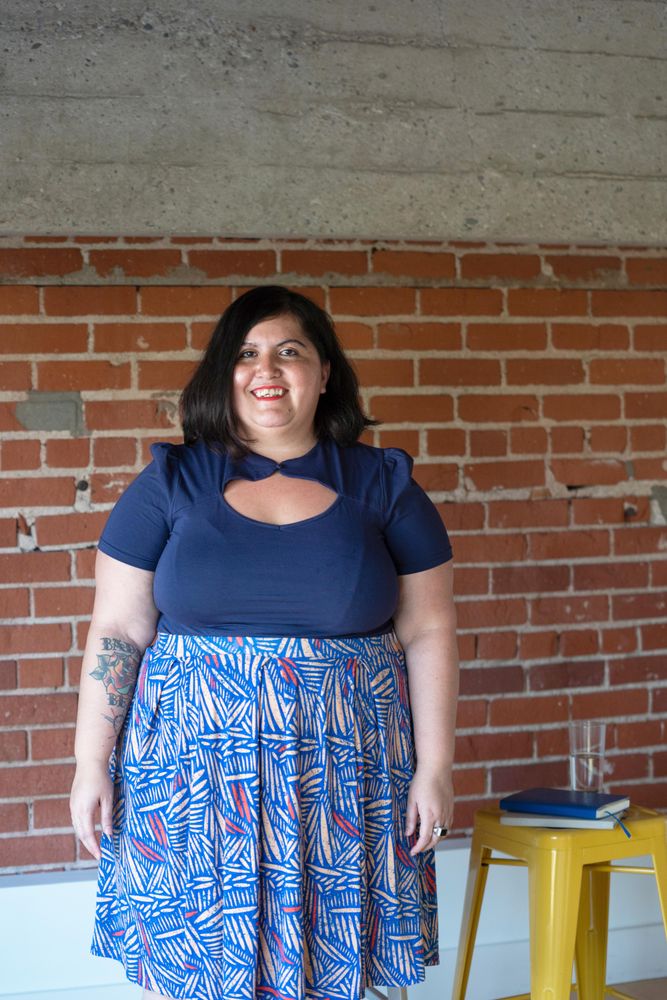 Woman with tattoos smiling in front of a brick wall