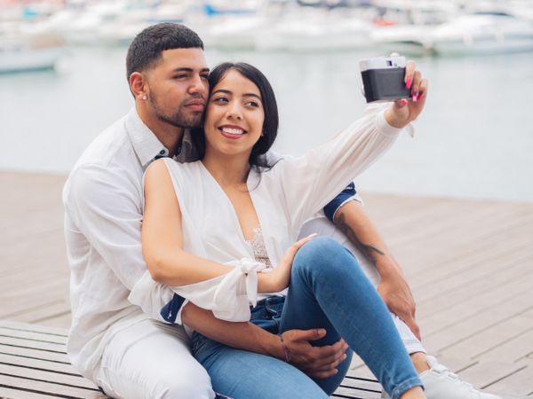 Woman with man taking photo selfie and sitting on bench