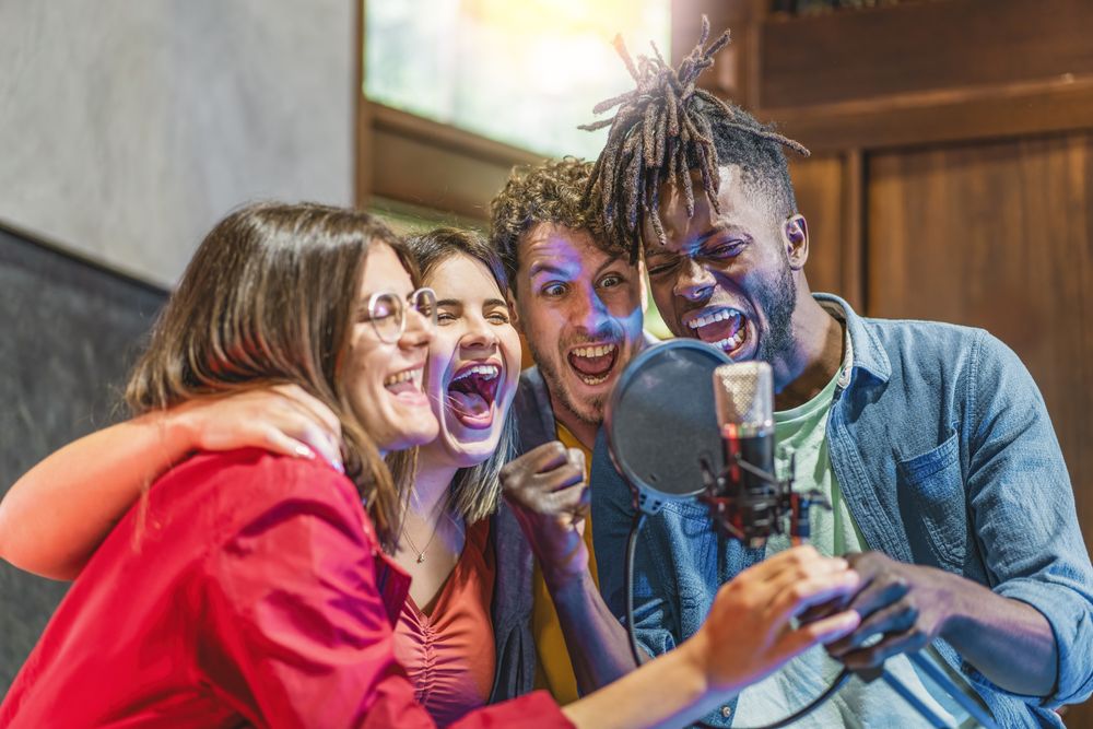 A diverse group of young men and women fervently singing around a condenser microphone