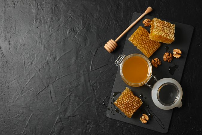 Walnut, honeycombs, jar with honey and dipper on dark background, copy space