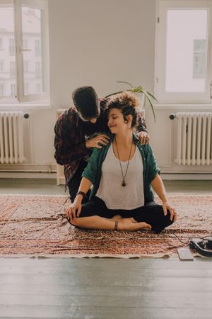 Man rubbing shoulders of joyful woman resting on floor at home