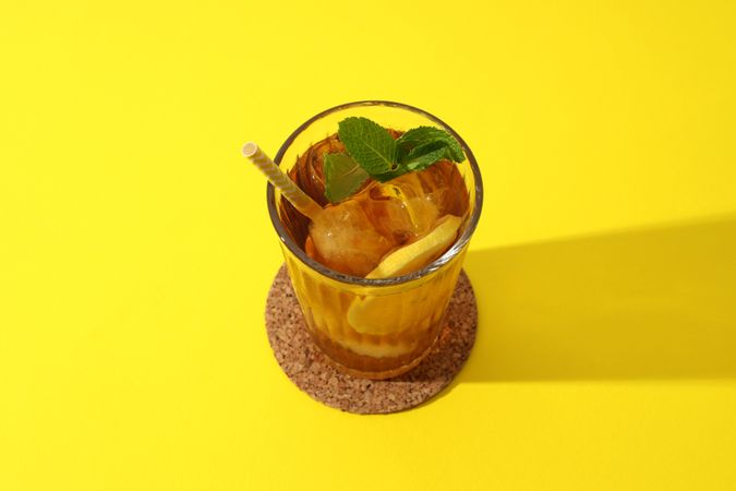 Cold tea with orange slices and mint leaves on a yellow background