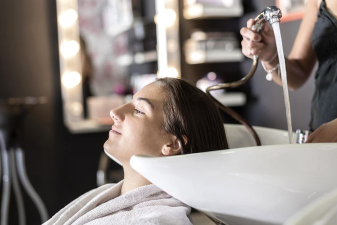 Female sitting with eyes closed and head back in sink at hairdressers having her hair washed