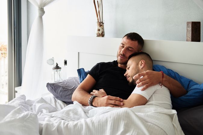 Smiling gay couple hugging on bed