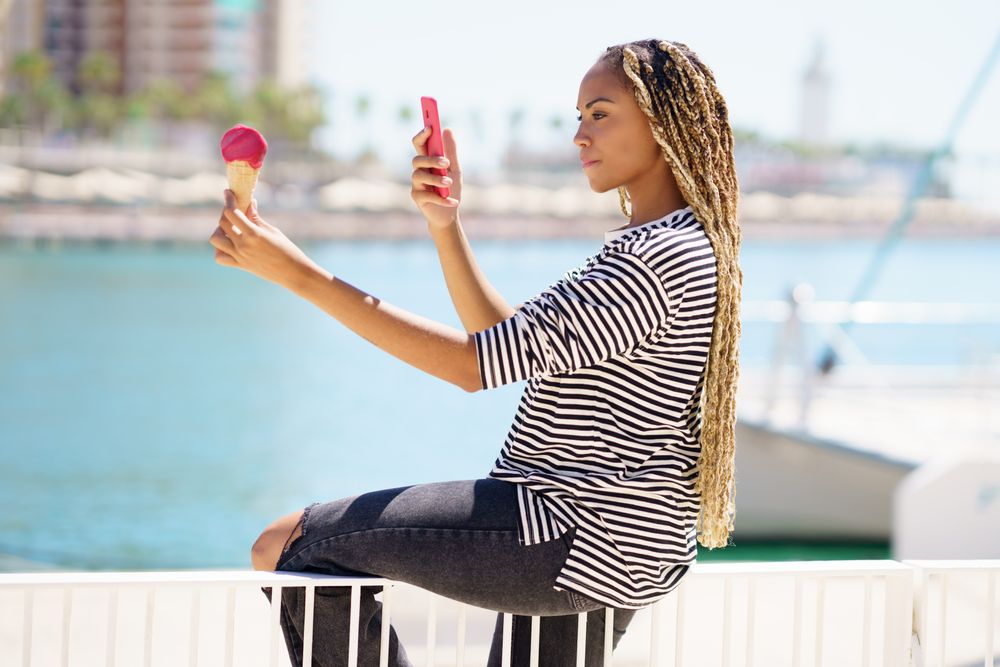 Female using smartphone to picture ice cream cone on the waterfront