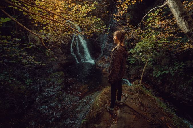 woman standing in a Small river and waterfall flowing in green dark beautiful forest.