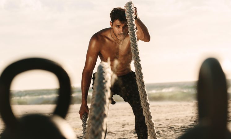 Shirtless male using arms to lift battle ropes for intense workout