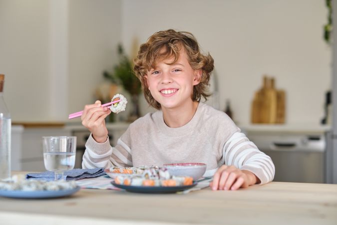 Cheerful kid enjoying delicious rolls in kitchen at home