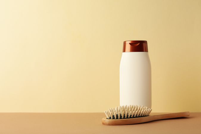Blank shampoo bottle and hair brush on beige background