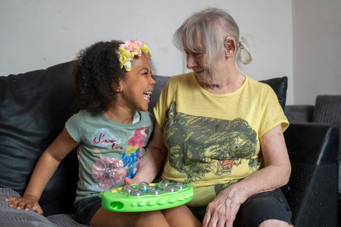 Older woman and grandchild laughing on coach at home