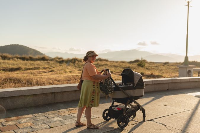 A young grandmother happily strolls her baby granddaughter, just a few months old, in her stroller during a sunny summer afternoon in a small village in northern Galicia, Spain