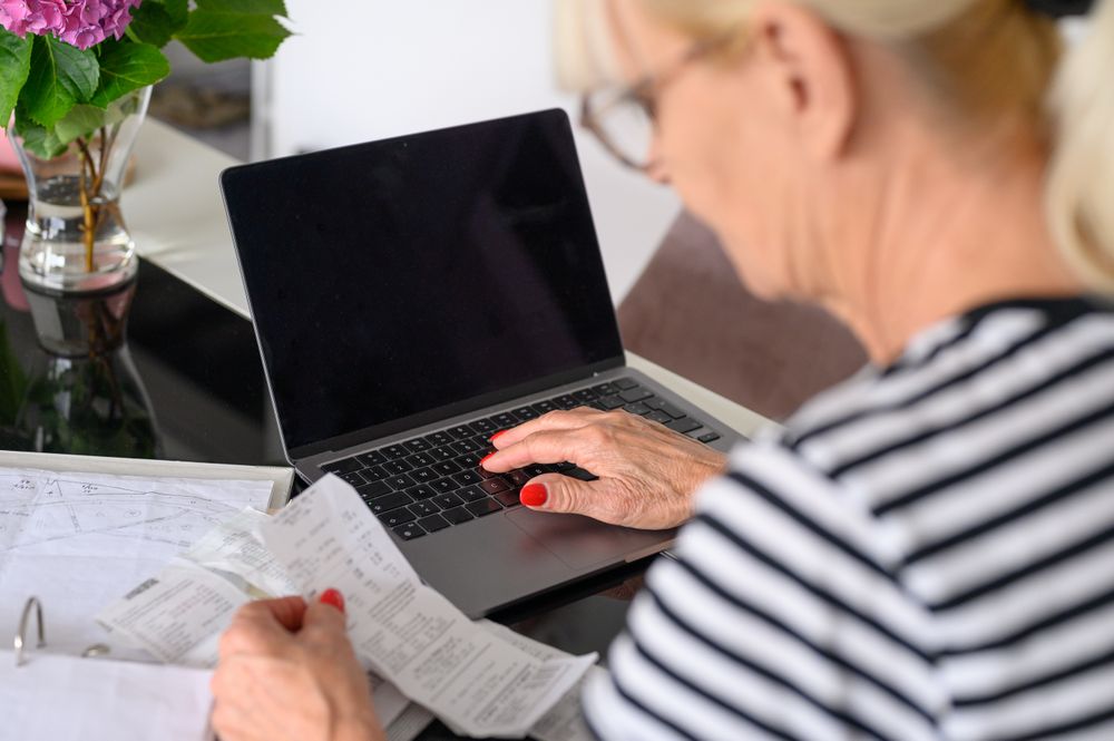 Mature woman watching bills and mail bank notice, sitting at living room table at home