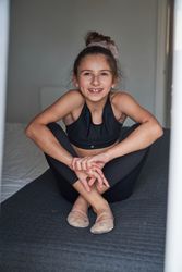 Smiling preteen gymnast in sportswear sitting on bed