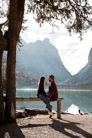 Male and female travelers sitting on fence near lake and mountains