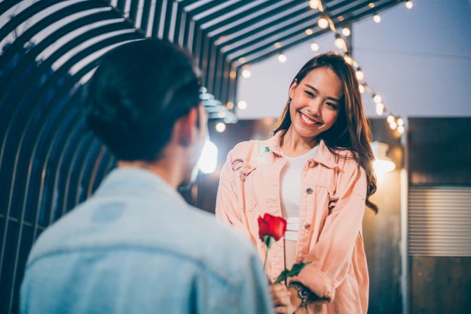 Asian man on knee giving rose and proposing to girlfriend on date night