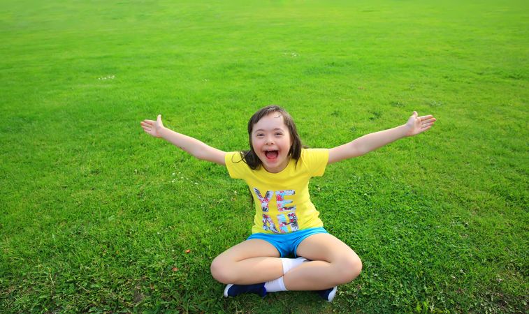 Young girl with Down syndrome sitting in a field with outstretched arms