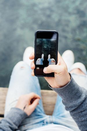 Close up of phone screen as man sits on pier taking photo