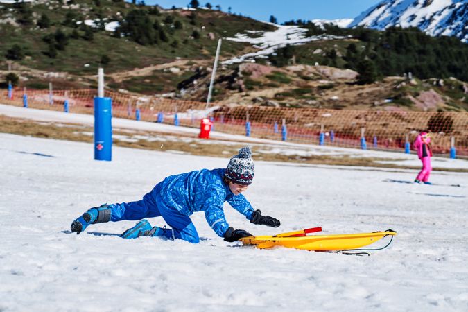 Happy boy crawling near sleigh in winter