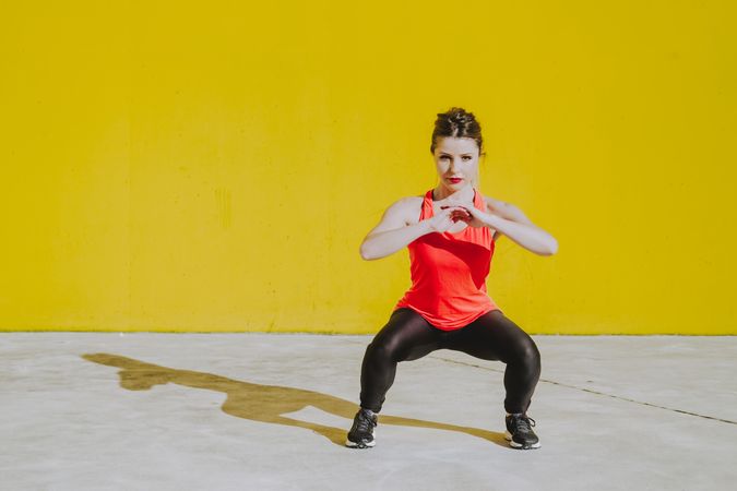 Woman doing squads exercises near a yellow wall