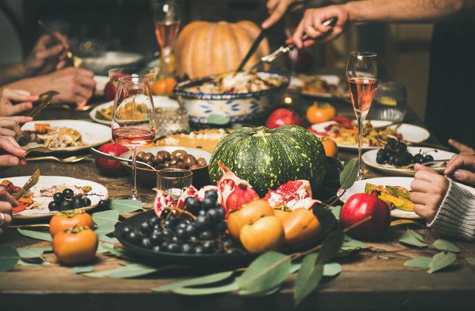 Group of people at festive fall dinner with wine, squash, olives, decorative roast pan