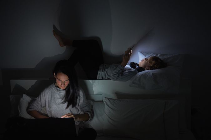 Woman and boy surfing gadgets in bedroom together