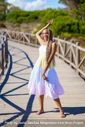 Smiling female looking at camera and walking on a pedestrian walkway in colorful dress bYLe14