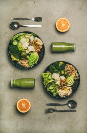 Two vegetarian bowls, with smoothie, orange halves, silverware, vertical composition