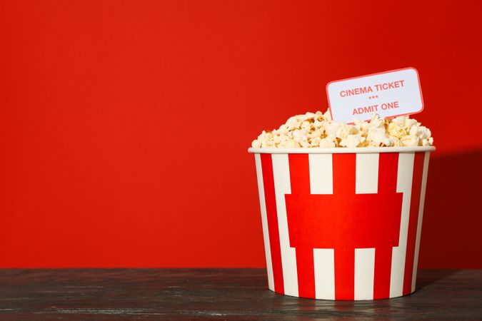 Striped bucket with popcorn and tickets against red background