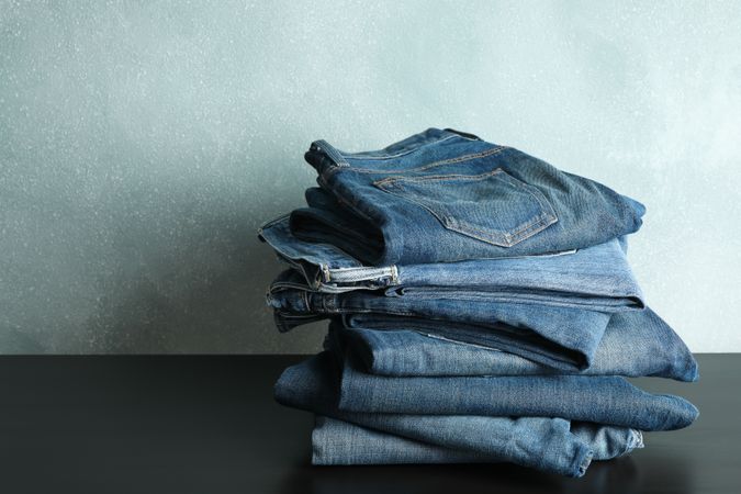 Stack of jeans pants on table, space for text