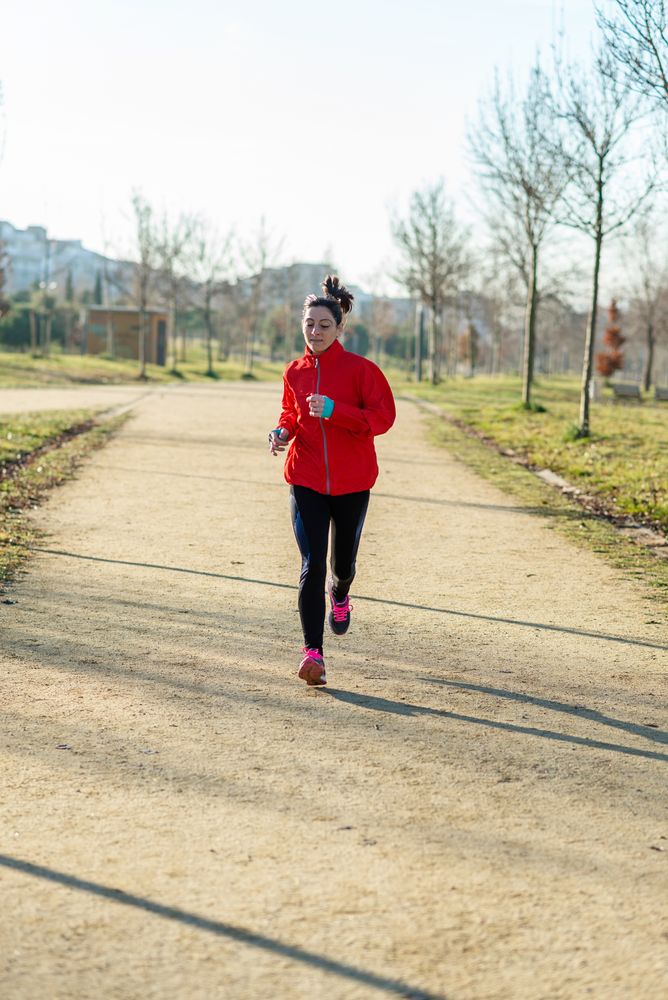Woman in red jogging outdoors in park on sunny autumn day