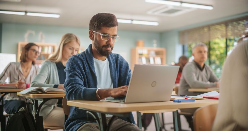 Indian Student Listening to Tutor and Writing Down Lecture on Laptop Computer in Class.
