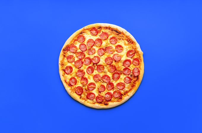 Top view with a whole pepperoni pizza isolated on a blue background