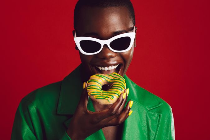 Fashionable woman eating donut on red background