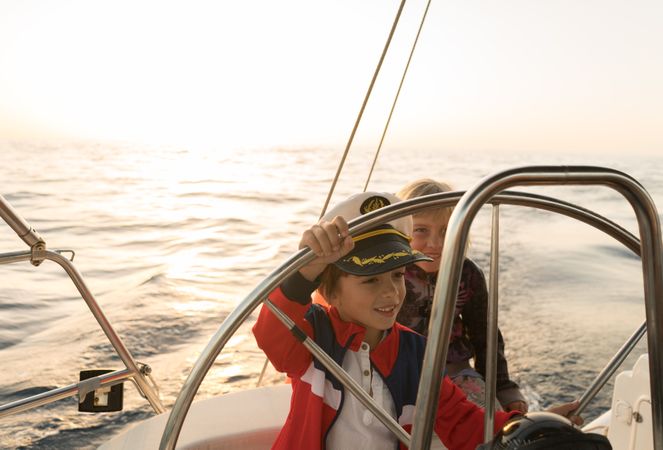 Smiling children holding steering wheel on yacht on water
