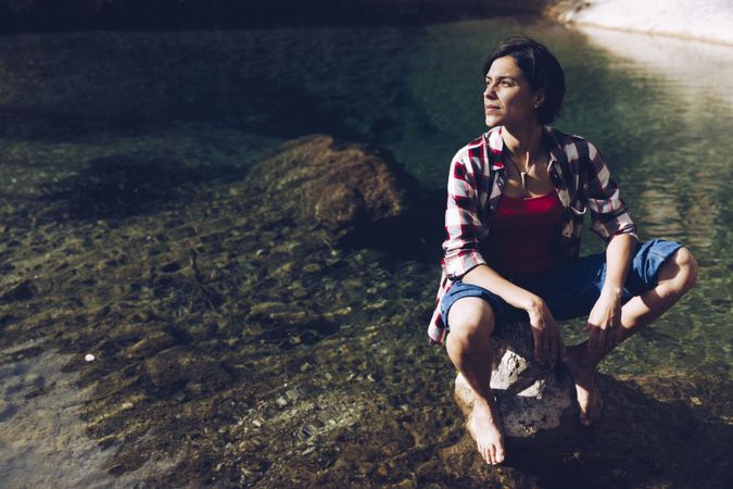 Cheerful woman sitting on rock in clear water