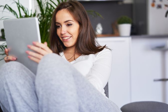 Smiling woman browsing on tablet and sitting on settee