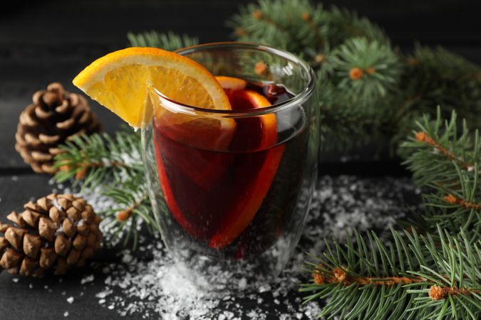 Glass of tasty mulled wine with orange on decorated wooden background, close up