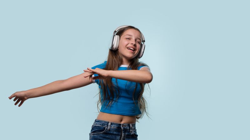 Girl in blue shirt wearing headphones while dancing.