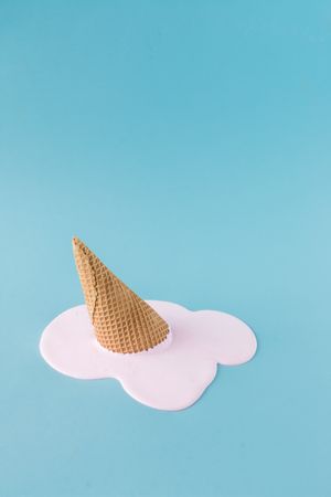 Melted pink ice cream and waffle cone on pastel blue background