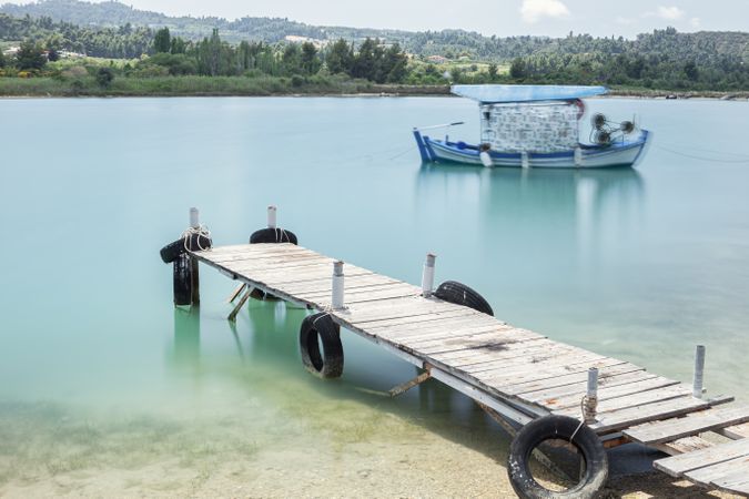 Wooden jetty with lifebuoys and sailing blue boat in calm water