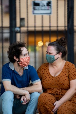 Happy partners sitting together in front of apartment building wearing masks