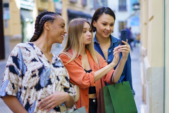 Smiling women on shopping trip taking picture of storefront