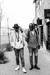 Two young male friends pose for a photo on the sidewalk in fashionable clothing